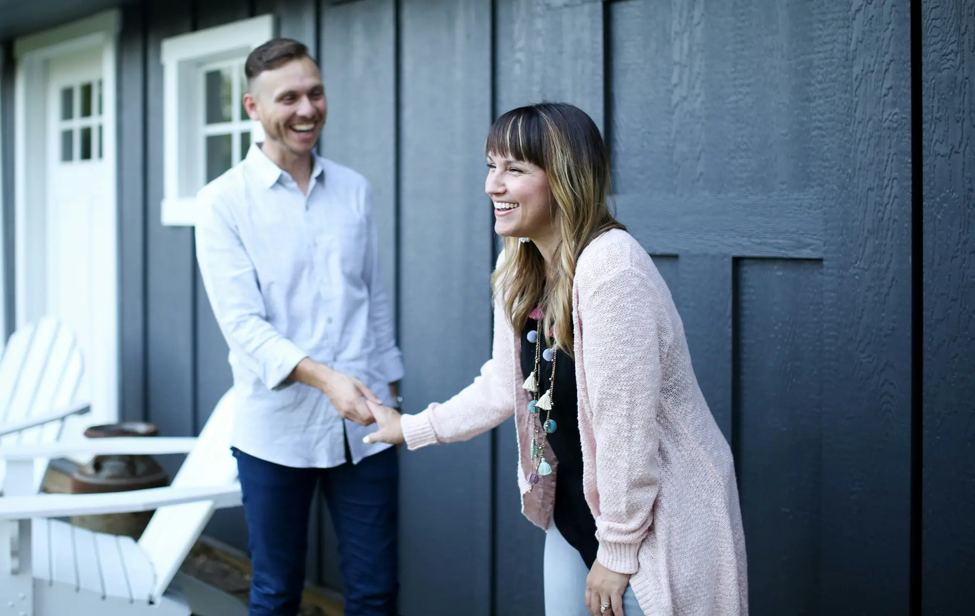 A man and a woman laugh as they shake hands outside the front of a house.