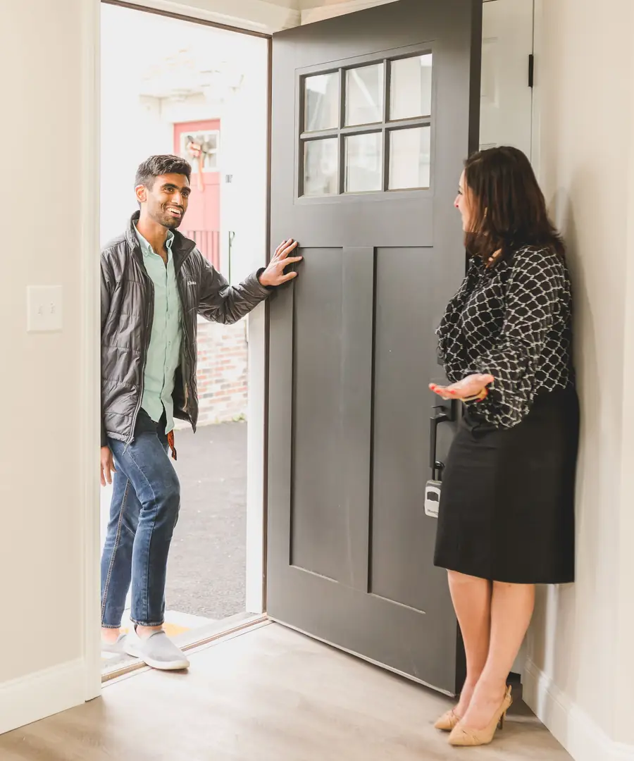 An agent holds the front door of a house for sale open as a buyer arrives for a showing.