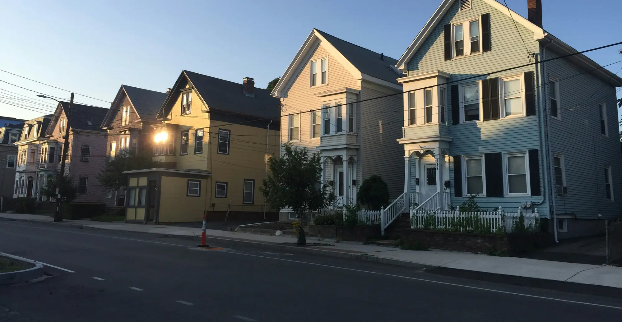 Two- and three-family clapboard houses along a city street in the last sun of the evening.
